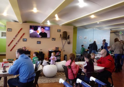 A cozy café scene with families enjoying food, a TV playing in the background, and colorful decor.
