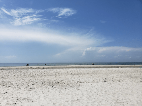 A serene beach scene with soft white sand, calm blue waters, and a clear sky with scattered clouds.