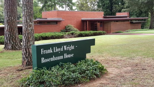 Sign for the Frank Lloyd Wright Rosenbaum House, with the house visible in the background surrounded by greenery.