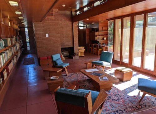 A cozy interior with bookshelves, a fireplace, and seating around a coffee table, featuring large windows and natural light.