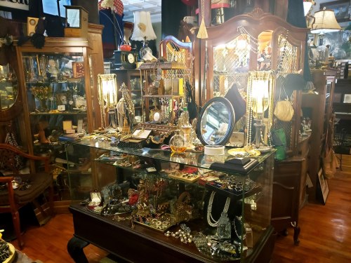 A vintage shop display filled with various jewelry pieces, mirrors, and decorative items under warm lighting.
