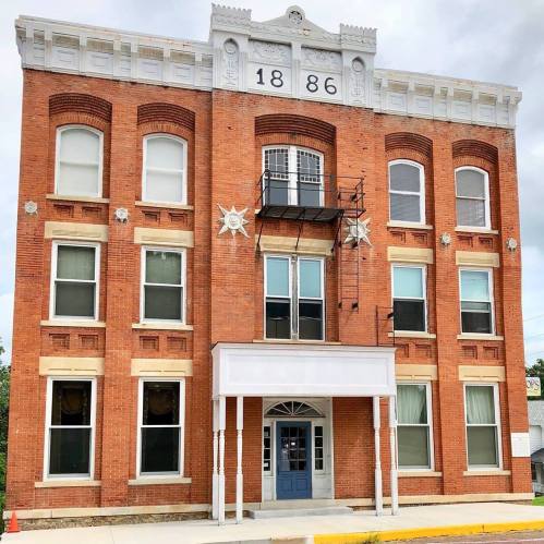 Historic red brick building with decorative elements, featuring large windows and a central entrance, dated 1886.