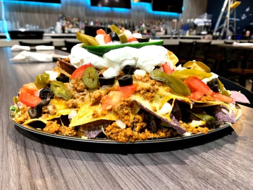 A large plate of nachos topped with ground beef, cheese, jalapeños, olives, tomatoes, and sour cream.