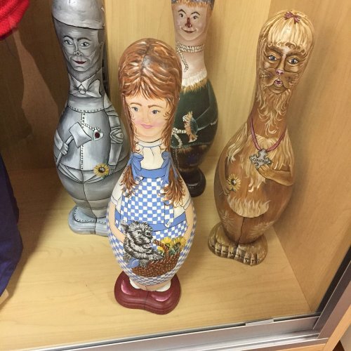 A display of decorative bowling pins, featuring painted characters including a girl with a basket and an animal figure.