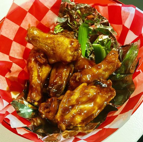 A basket lined with red and white checkered paper filled with glazed chicken wings and celery sticks.
