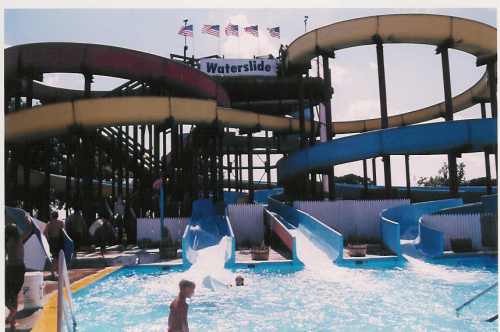A water park featuring colorful waterslides and a pool, with people enjoying the attractions under a sunny sky.