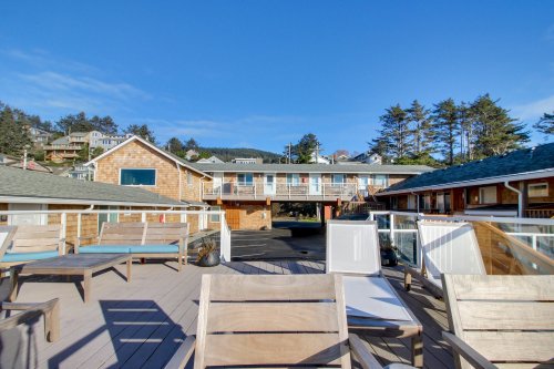 A sunny outdoor area with wooden chairs, overlooking a building and trees in a coastal setting.