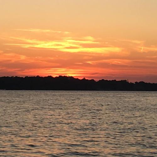 A vibrant sunset over a calm body of water, with orange and pink hues reflecting on the surface.