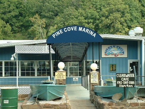 Entrance to Pine Cove Marina, featuring a blue awning and boats in front, surrounded by greenery.