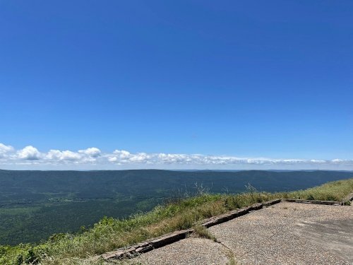 A panoramic view of green mountains under a clear blue sky with scattered clouds.