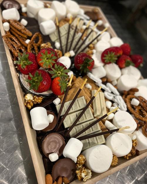 A wooden platter filled with strawberries, marshmallows, pretzels, chocolate, popcorn, and assorted snacks.