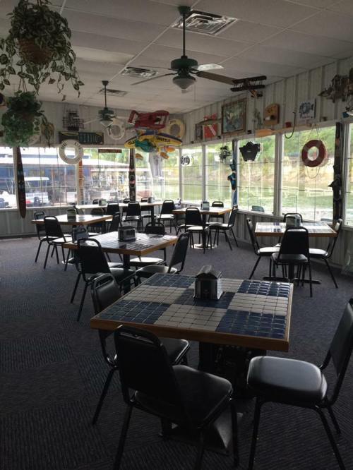 A cozy restaurant interior with empty tables, green chairs, and nautical decor on the walls and ceiling.
