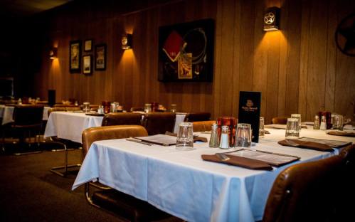 Cozy restaurant interior with wooden walls, white tablecloths, and empty tables set for dining.