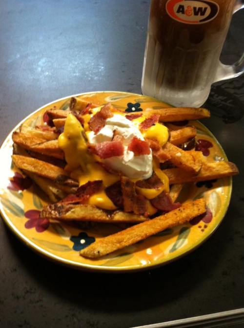 A plate of loaded fries topped with cheese, bacon, and sour cream, alongside a frosty mug of root beer.