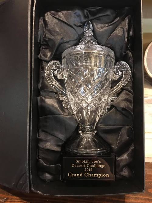 A crystal trophy in a black box, labeled "Smokin' Joe's Dessert Challenge 2019 Grand Champion."