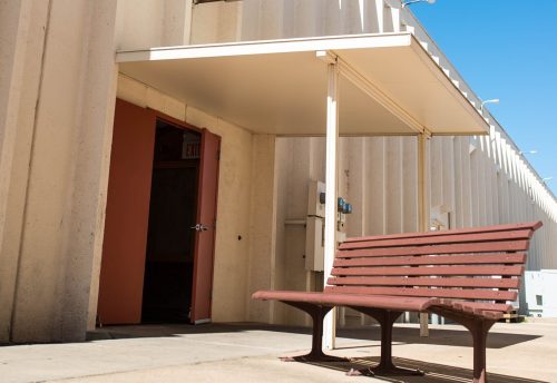 Sign for "Rusty Barrell Supper Club" above a bench outside a building with a clear blue sky.