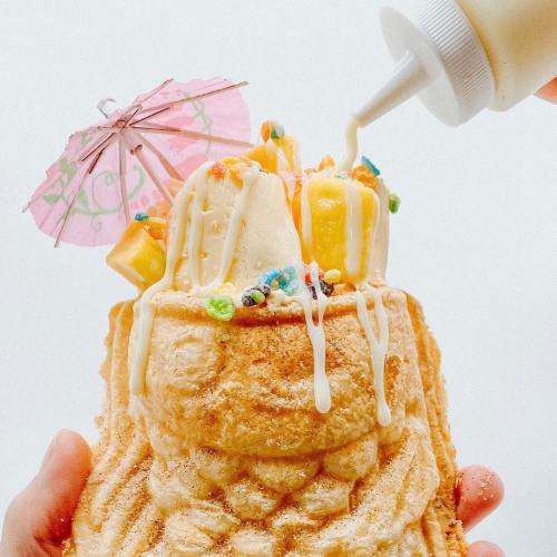 A colorful ice cream sundae in a waffle cone, topped with sprinkles, an umbrella, and drizzled with sauce.