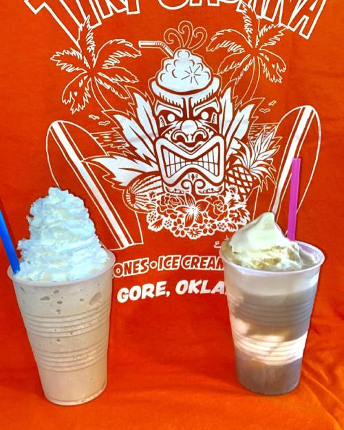 Two cups of ice cream drinks topped with whipped cream, set against an orange shirt featuring a tiki design.