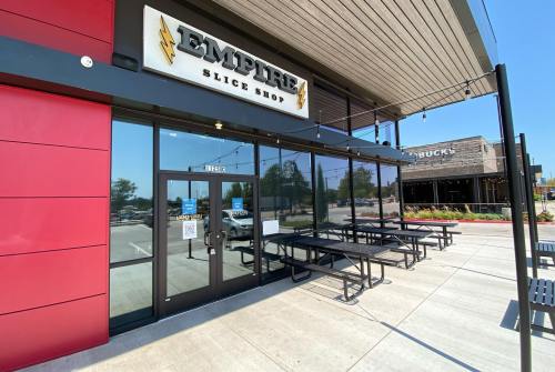 Exterior of Empire Slice Shop with a modern design, featuring outdoor seating and a clear blue sky.