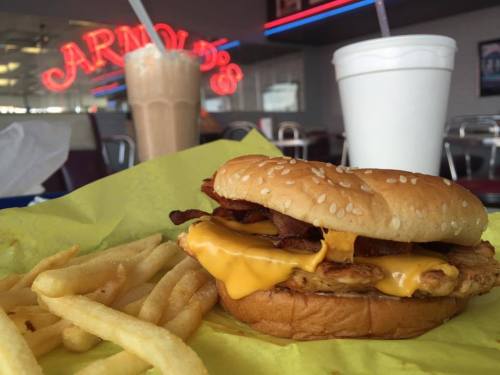 A cheeseburger with bacon and fries on a yellow plate, with milkshakes in the background at a diner.
