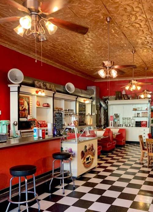 A vintage-style café with red walls, checkered floor, and retro seating, featuring a display of ice cream and desserts.