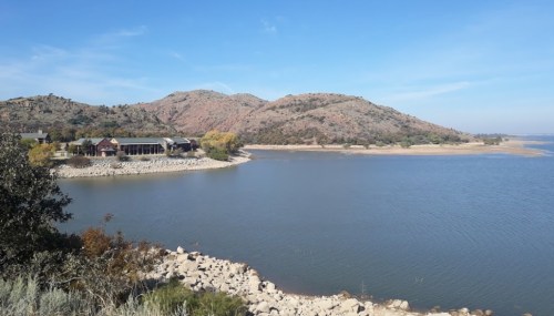 Scenic view of a calm lake surrounded by hills and a building along the shore under a clear blue sky.
