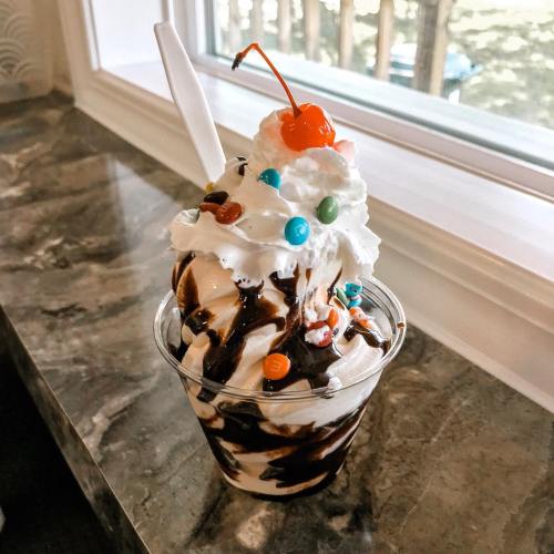 A delicious ice cream sundae topped with whipped cream, chocolate sauce, colorful candies, and a cherry.
