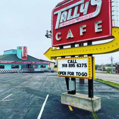 Sign for Tally's Cafe with a retro design, indicating it's open for takeout. Empty parking lot in the background.
