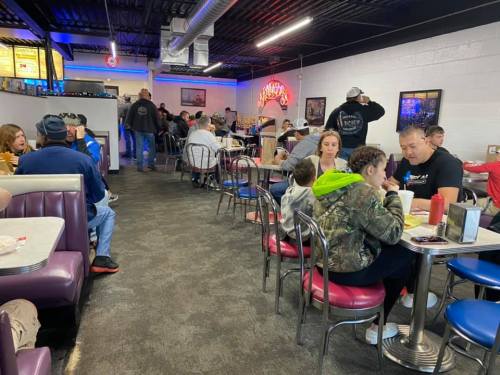 A busy diner with patrons seated at tables, enjoying meals in a casual, colorful setting.