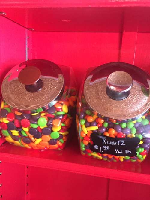 Two glass jars filled with colorful candies, labeled "Runts," on a red shelf. Price: $1.95 per quarter pound.