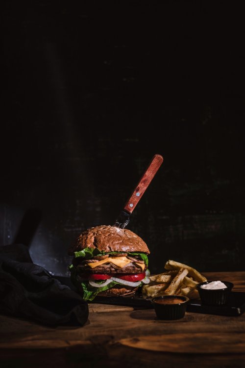 A gourmet burger with lettuce, tomato, and cheese, served with fries and dipping sauces on a wooden table.