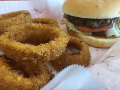A plate with crispy onion rings next to a hamburger with lettuce and tomato on a bun.