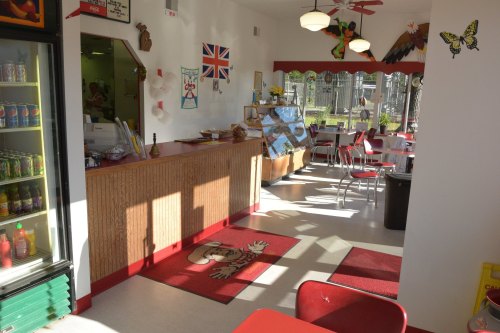 A colorful diner interior with red accents, a counter, tables, and a vintage decor featuring butterflies and a British flag.
