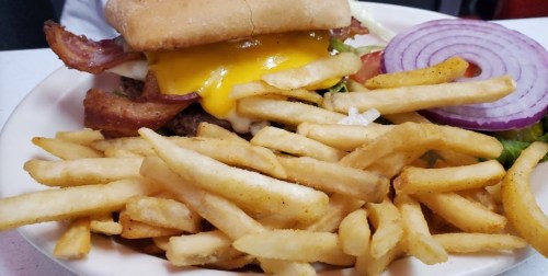 A close-up of a cheeseburger topped with bacon, lettuce, and tomato, served with a side of golden French fries.