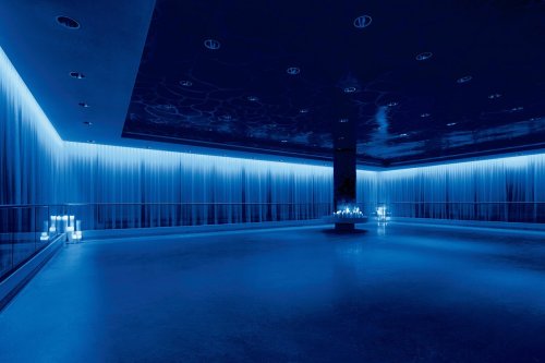 A dimly lit room with blue lighting, featuring sheer curtains and a central column, creating a modern, serene atmosphere.