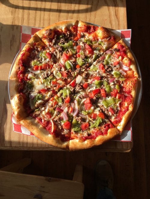 A freshly baked pizza topped with cheese, tomatoes, green peppers, onions, and ground meat, sliced into eight pieces.