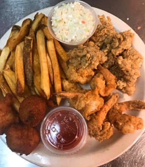 A plate of fried chicken, coleslaw, French fries, hushpuppies, and dipping sauce.