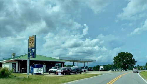 A roadside view of a gas station with several cars parked outside under a cloudy sky.