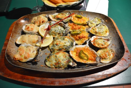 A platter of baked oysters topped with various ingredients, garnished with lemon slices and a red skewer.