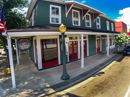 A green two-story building with a sign reading "Wintzell's Oyster House," featuring red accents and a sunny sky.