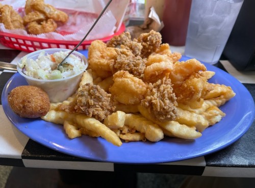 A blue plate filled with fried shrimp, fries, coleslaw, and a cornbread muffin.
