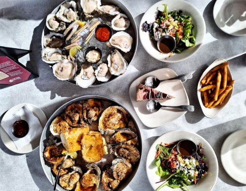 A spread of seafood including oysters, fried oysters, salads, fries, and dessert on a table.