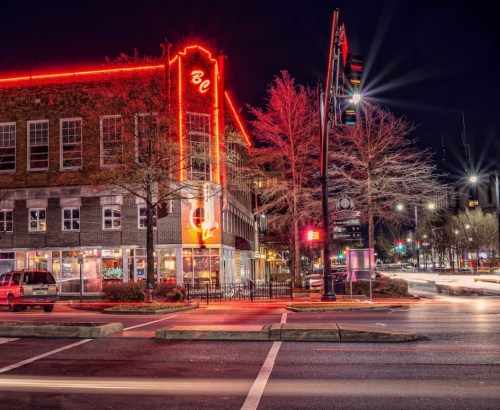 A brightly lit building at night with neon signs, surrounded by trees and streetlights in a bustling urban area.