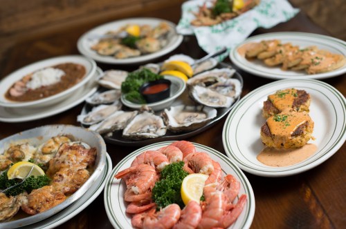 A variety of seafood dishes including shrimp, oysters, and crab cakes, arranged on plates with garnishes.