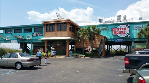 Exterior of the Oyster House restaurant with palm trees, cars parked, and people walking towards the entrance.