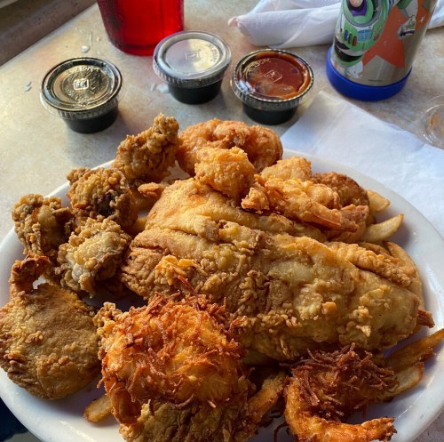 A plate of fried chicken and shrimp with dipping sauces, served with a side of fries.