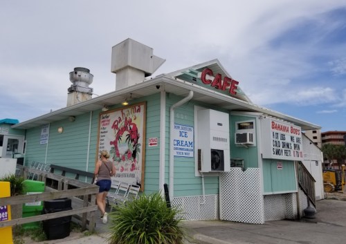 A pastel-colored café with a sign reading "Cafe" and "Bahamaboo's," featuring outdoor seating and a beachy vibe.
