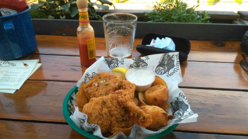 A basket of fried chicken with dipping sauce, lemon, and hushpuppies, alongside a glass of beer and hot sauce.