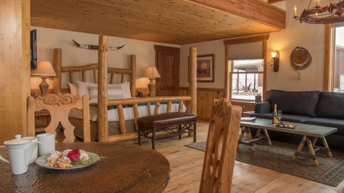 Cozy cabin interior featuring a wooden bed, seating area, and dining table with snacks and drinks. Warm, rustic decor.