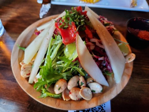 A colorful salad topped with sliced pears, tomatoes, and nuts, served on a wooden plate.